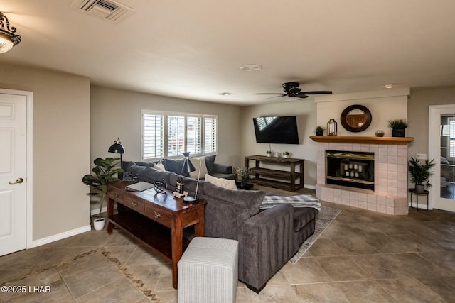 tiled living area with ceiling fan, a tiled fireplace, visible vents, and baseboards