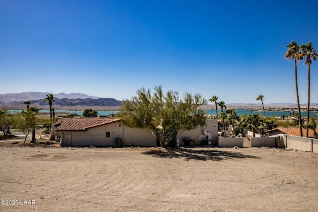 view of front of property featuring a water and mountain view, fence, a tiled roof, and stucco siding