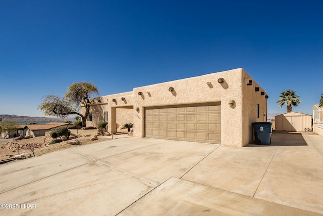 pueblo-style home with a garage, concrete driveway, an outdoor structure, and stucco siding