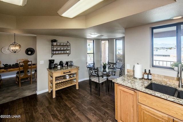 kitchen with a chandelier, light stone counters, dark wood-style flooring, a sink, and baseboards