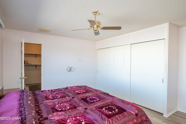 bedroom with a textured ceiling, ceiling fan, visible vents, a closet, and light wood-type flooring