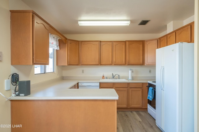 kitchen with light countertops, visible vents, a sink, white appliances, and a peninsula