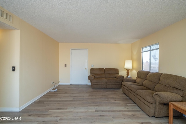 living room featuring baseboards, visible vents, a textured ceiling, and light wood finished floors