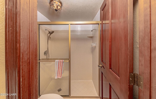 bathroom featuring a shower with shower door, toilet, and a textured ceiling