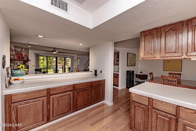 kitchen with ceiling fan, tile counters, a textured ceiling, and light hardwood / wood-style floors