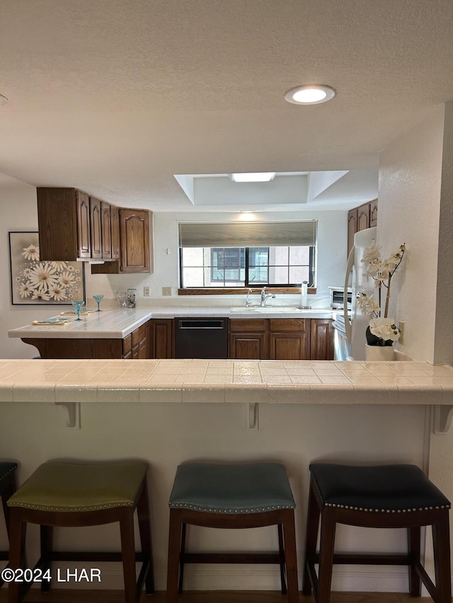 kitchen featuring black dishwasher, a breakfast bar area, white fridge, kitchen peninsula, and a textured ceiling