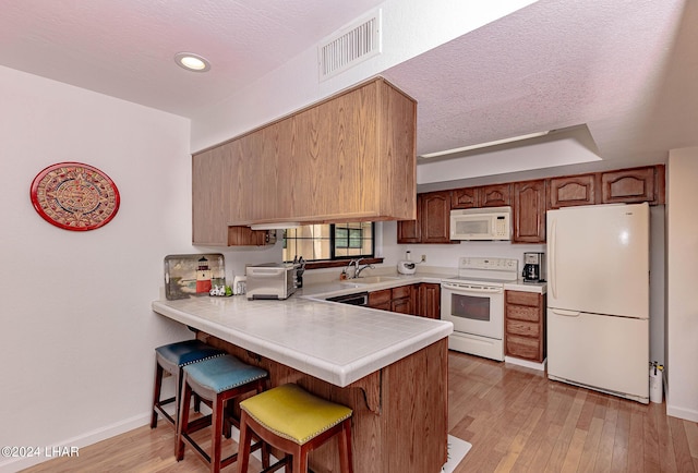 kitchen featuring sink, white appliances, light hardwood / wood-style flooring, and kitchen peninsula