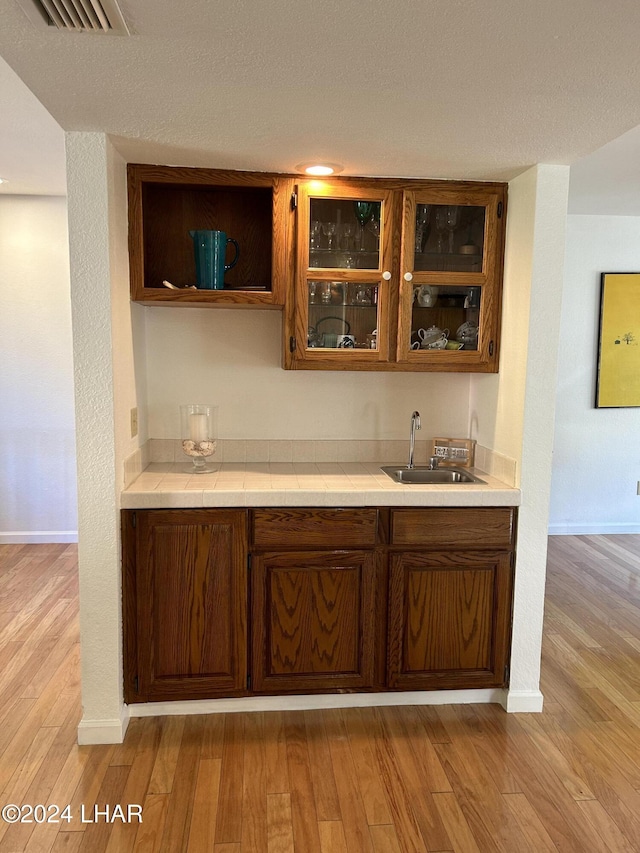 bar with sink, a textured ceiling, and light wood-type flooring