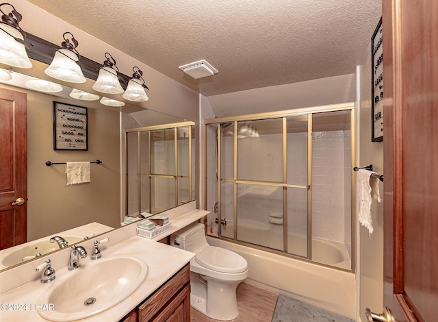 full bathroom with bath / shower combo with glass door, wood-type flooring, vanity, toilet, and a textured ceiling