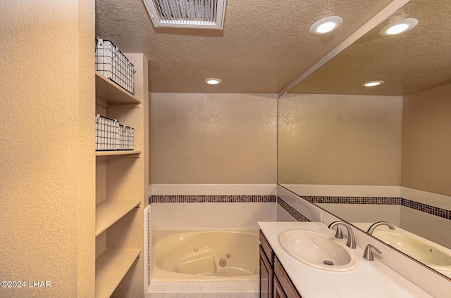 bathroom featuring tiled tub, vanity, and a textured ceiling