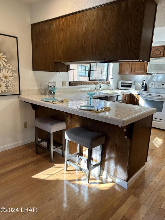 kitchen featuring a kitchen breakfast bar, light wood-type flooring, white appliances, and kitchen peninsula