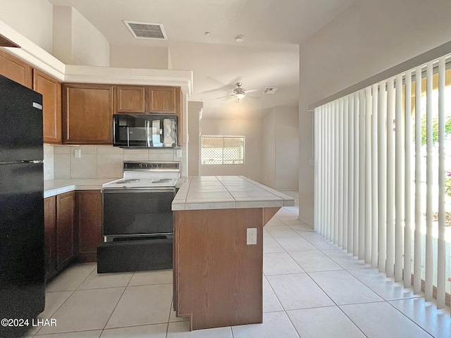 kitchen with light tile patterned flooring, decorative backsplash, a center island, tile counters, and black appliances