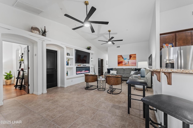 living area featuring visible vents, built in shelves, a glass covered fireplace, arched walkways, and lofted ceiling