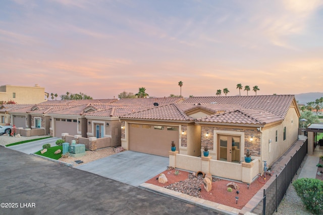 mediterranean / spanish house featuring stucco siding, stone siding, fence, a garage, and a tiled roof