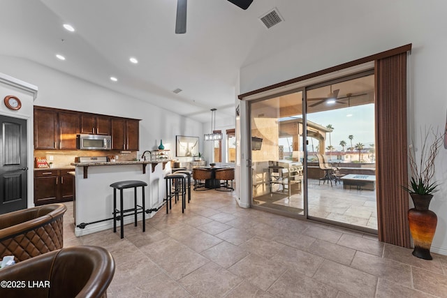 kitchen with stainless steel microwave, a kitchen breakfast bar, a ceiling fan, and visible vents