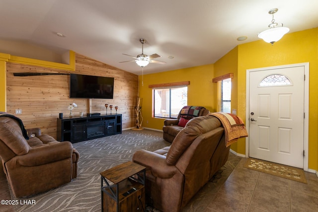 living area with baseboards, ceiling fan, wood walls, lofted ceiling, and tile patterned floors