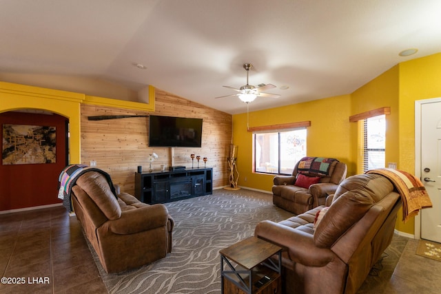 tiled living area featuring lofted ceiling, wood walls, a fireplace, baseboards, and ceiling fan