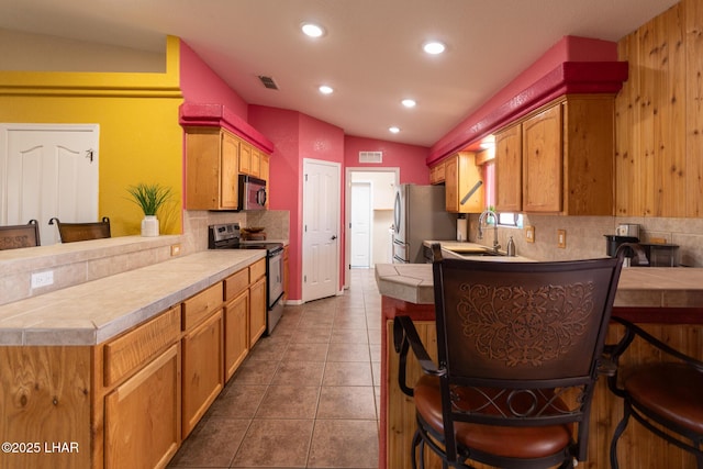 kitchen featuring visible vents, a peninsula, tile patterned flooring, decorative backsplash, and appliances with stainless steel finishes