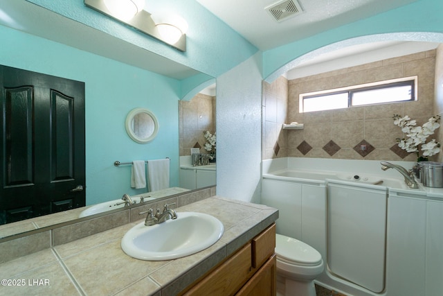 full bathroom featuring visible vents, toilet, vanity, and a tub with jets