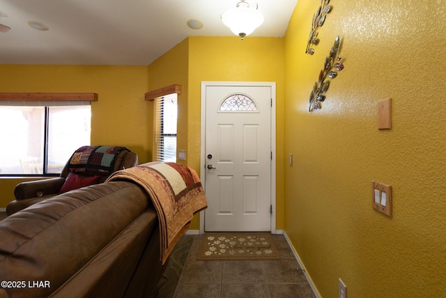 entryway with dark tile patterned floors, a textured wall, and baseboards