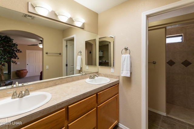 full bath with a sink, visible vents, tiled shower, and double vanity