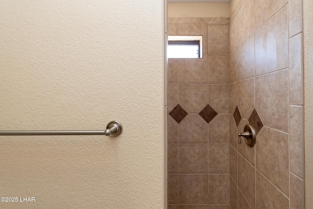 room details featuring tiled shower and a textured wall