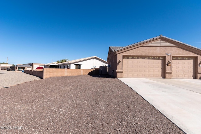 view of front of home featuring fence, a tiled roof, concrete driveway, stucco siding, and an attached garage