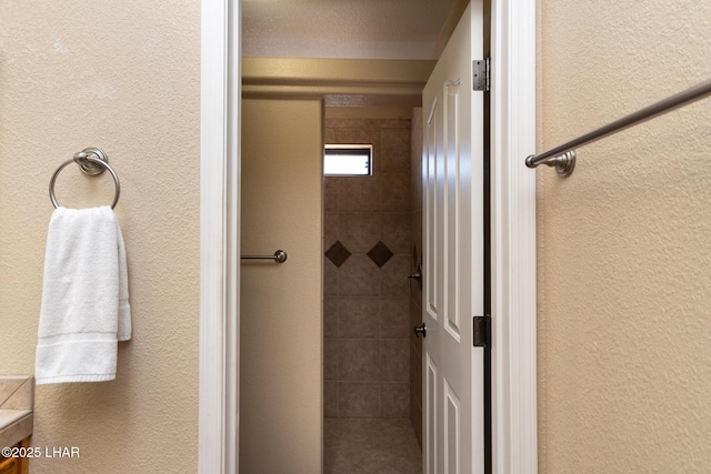 bathroom with tiled shower and a textured wall