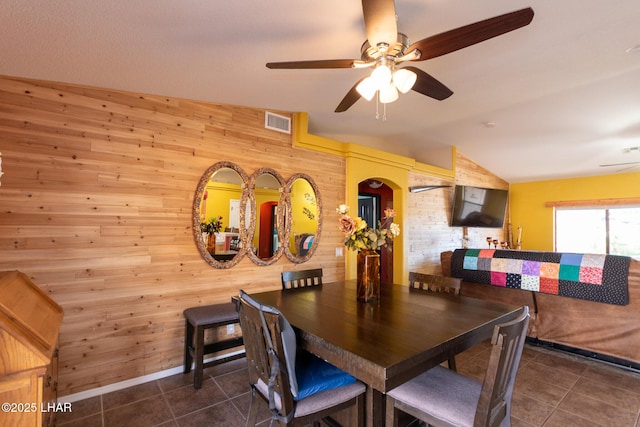 tiled dining room with visible vents, lofted ceiling, wood walls, and a ceiling fan