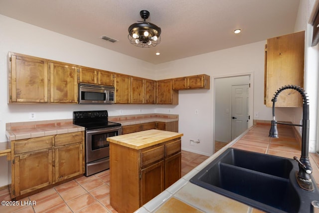 kitchen with brown cabinets, stainless steel appliances, light tile patterned floors, a sink, and butcher block counters