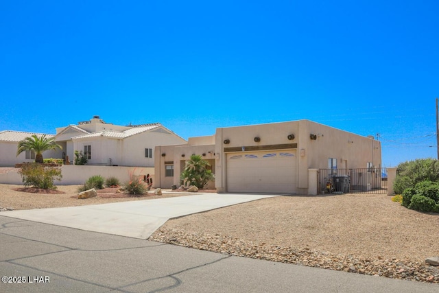 pueblo-style home featuring a chimney, fence, stucco siding, an attached garage, and concrete driveway