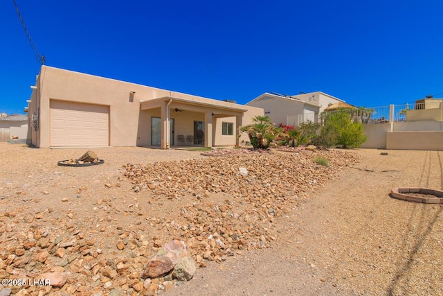 view of front facade with an attached garage, a ceiling fan, fence, and stucco siding