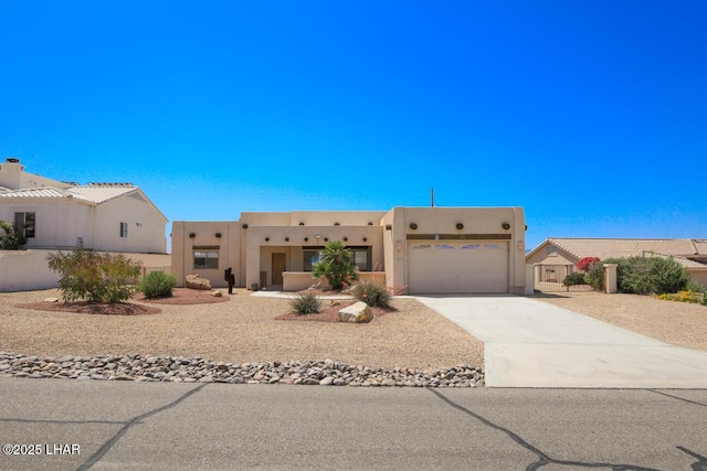 pueblo revival-style home featuring an attached garage, driveway, and stucco siding