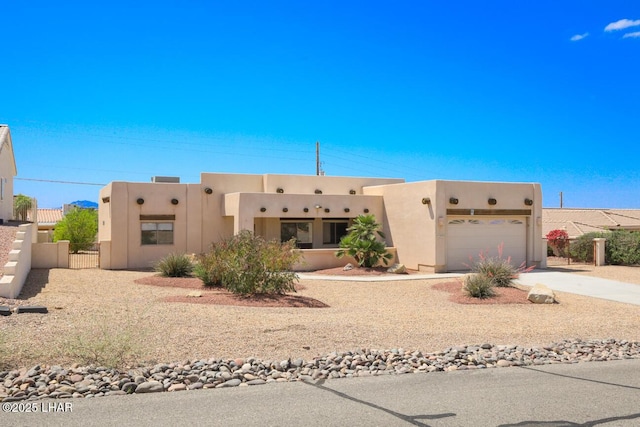 southwest-style home featuring an attached garage, concrete driveway, stucco siding, and fence