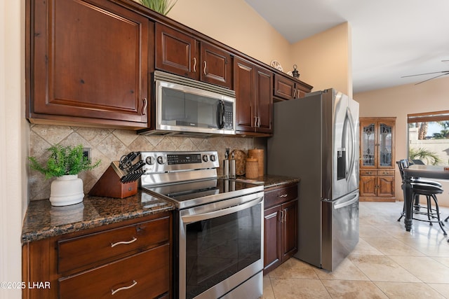 kitchen with appliances with stainless steel finishes, tasteful backsplash, dark stone countertops, light tile patterned floors, and ceiling fan