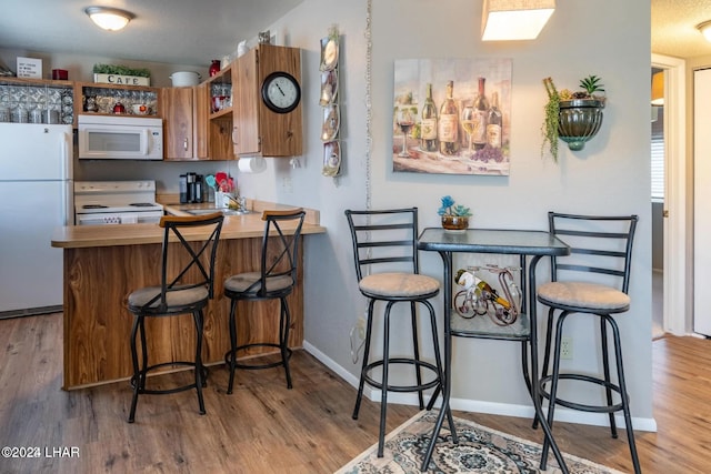 kitchen with a kitchen breakfast bar, light wood-type flooring, white appliances, and kitchen peninsula