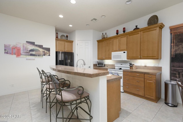 kitchen with white appliances, a center island with sink, visible vents, a kitchen breakfast bar, and light countertops