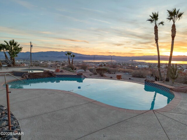 pool at dusk with a mountain view, a patio area, and an in ground hot tub