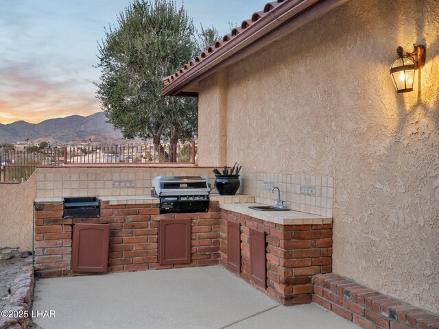 patio terrace at dusk with area for grilling, a mountain view, grilling area, and sink