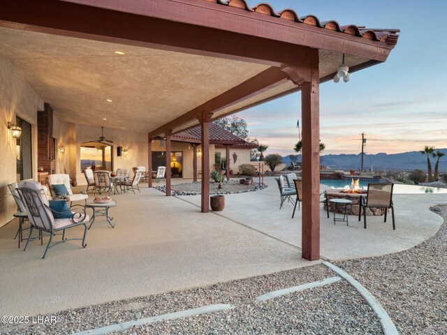 patio terrace at dusk featuring a mountain view, ceiling fan, and an outdoor fire pit