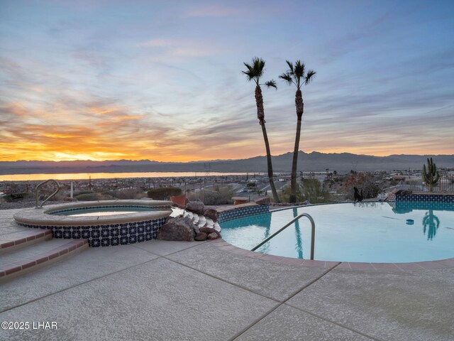 pool at dusk featuring a mountain view, a patio, and an in ground hot tub