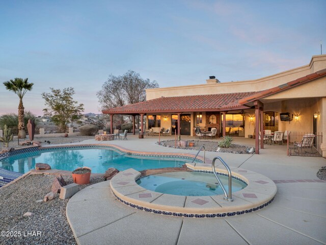 pool at dusk with a patio area and an in ground hot tub