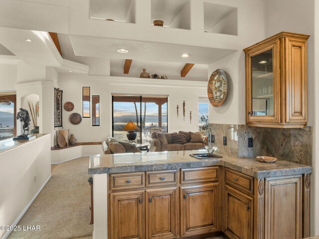 kitchen featuring sink, backsplash, light colored carpet, kitchen peninsula, and beam ceiling