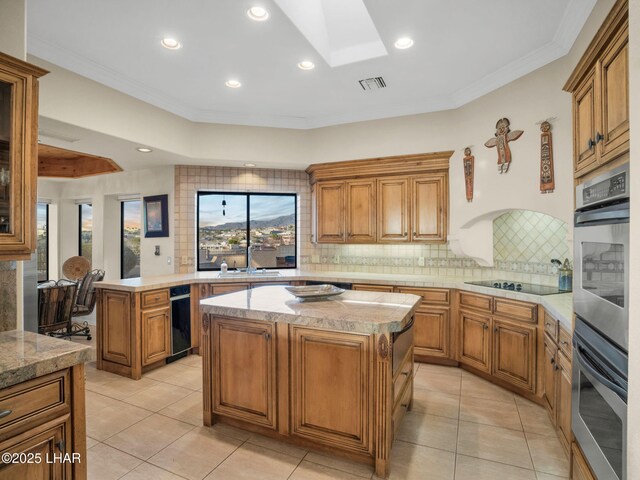 kitchen with a kitchen island, a skylight, tasteful backsplash, ornamental molding, and black electric cooktop