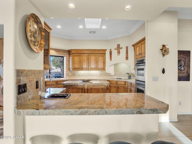 kitchen featuring double oven, tasteful backsplash, sink, a breakfast bar area, and kitchen peninsula