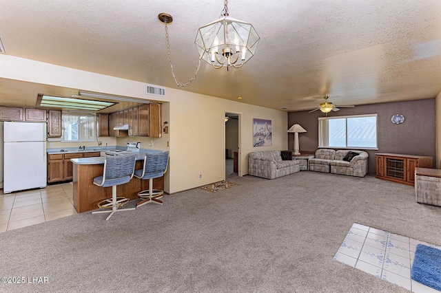 living room featuring ceiling fan with notable chandelier, light colored carpet, and a textured ceiling