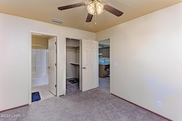 unfurnished bedroom with connected bathroom, a walk in closet, light colored carpet, ceiling fan, and a closet