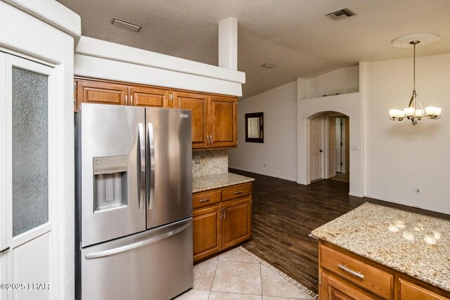 kitchen with stainless steel refrigerator with ice dispenser, light stone counters, vaulted ceiling, light tile patterned floors, and pendant lighting