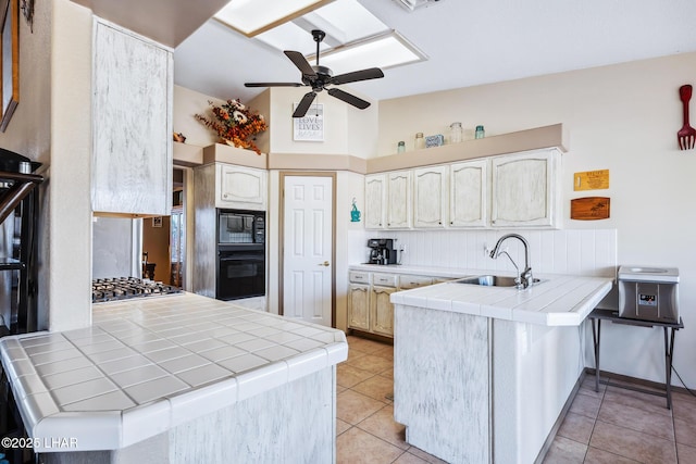 kitchen with a sink, tile counters, a ceiling fan, a peninsula, and black appliances