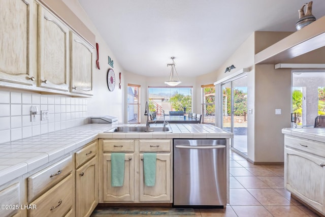 kitchen with a sink, dishwasher, tile counters, a peninsula, and tasteful backsplash